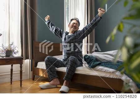 A man in his 50s sitting on the bed and stretching 110254820
