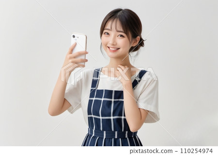 A beautiful housewife wearing an apron smiles while operating a smartphone 110254974