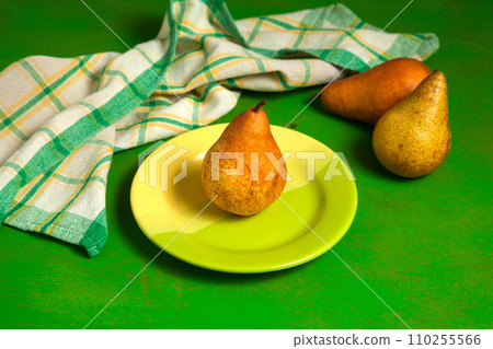 Green plate with pear and green kitchen towel on green wooden background.. 110255566