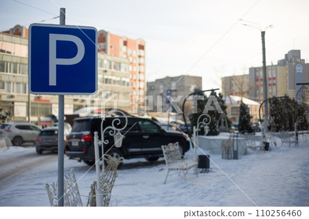 Road square blue sign with the letter "P" indicating a parking area near the park in the snow. Winter street in a city parking lot 110256460