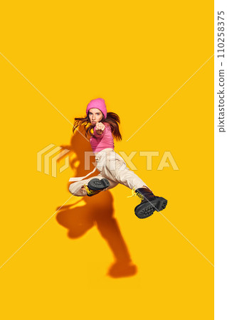 Urban chic in motion. Dynamic portrait of young woman, fashion-forward, posing in air against vivid yellow background. Concept of sales season. 110258375