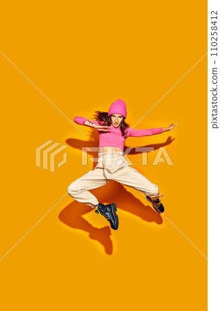 Dynamic full length portrait of attractive young girl, dressed fashion outfit jumping and posing in motion against vivid yellow background. Concept of style. Dynamic full length portrait of attractive young girl, dressed fashion outfit jumping and posing in motion against vivid yellow background. Concept of style. 110258412