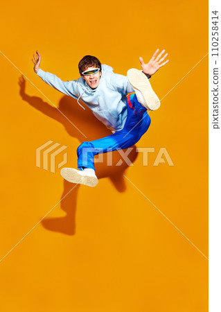 Full length portrait of young man dressed in the latest fashion jumps on a bright yellow background, realizing fusion of style and movement. Full length portrait of young man dressed in the latest fashion jumps on a bright yellow background, realizing fusion of style and movement. 110258414
