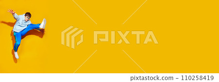 Young attractive man, dressed in comfy sportwear jumping in motion against vivid yellow background with negative space for text. Young attractive man, dressed in comfy sportwear jumping in motion against vivid yellow background with negative space for text. 110258419
