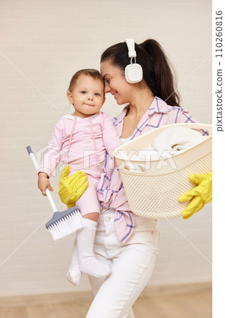 happy mother housewife is holding cute little child girl and basket with laundry and doing housework , Happy family 110260816