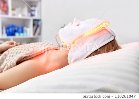 Woman lies with led light therapy facial mask in beauty salon Woman lies with led light therapy facial mask in beauty salon 110261047