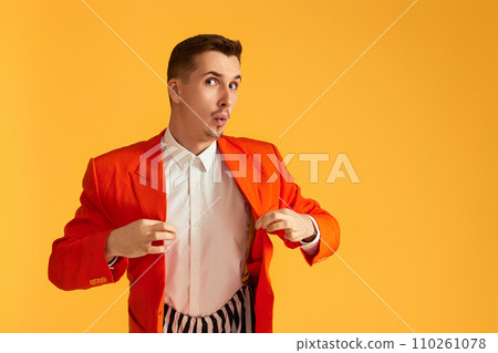 Cheerful funny young man in orange jacket and striped pants on yellow background. 110261078