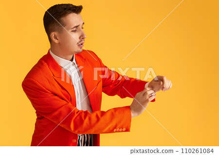 fashionable young man in orange jacket and striped pants on yellow background. 110261084