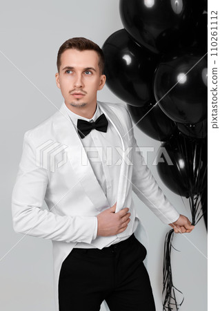 elegant caucasian man in white suit tuxedo with black air balloons on white background. 110261112