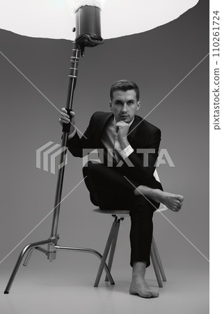 elegant model man in black suit barefoot in photostudio. black and white elegant model man in black suit barefoot in photostudio. black and white 110261724