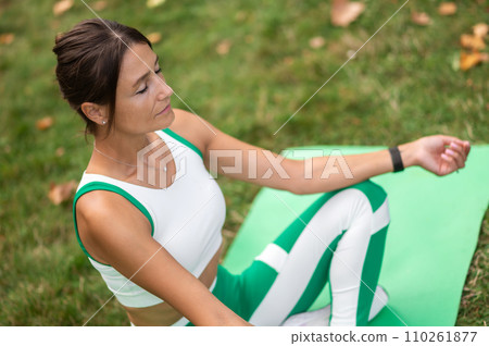 Woman in green sportswear sitting in a lotus pose and meditating Woman in green sportswear sitting in a lotus pose and meditating 110261877