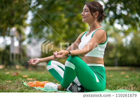 Woman in green sportswear sitting in a lotus pose and meditating Woman in green sportswear sitting in a lotus pose and meditating 110261879