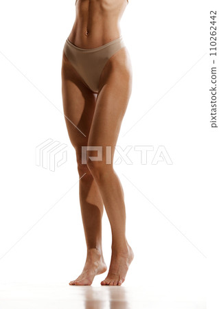 Cropped image of slender, tanned, smooth female legs. Model posing in beige cotton underwear against white studio background Cropped image of slender, tanned, smooth female legs. Model posing in beige cotton underwear against white studio background 110262442