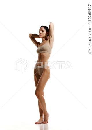 Full-length image of young woman with slim relief tanned body standing in beige cotton underwear against white studio background Full-length image of young woman with slim relief tanned body standing in beige cotton underwear against white studio background 110262447