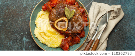 Traditional Italian dish Ossobuco all Milanese made with cut veal shank meat with vegetable tomato sauce served with corn polenta on ceramic plate top view on rustic stone background 110262753