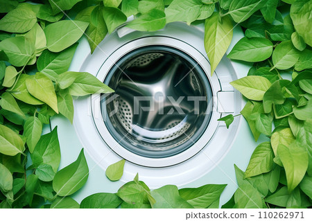 Washing machine with green leaves in it. Eco cleaning, eco friendly washing concept. Environmentally friendly bio natural home cleaning. Plants near modern washing machine. Spring cleaning theme. 110262971
