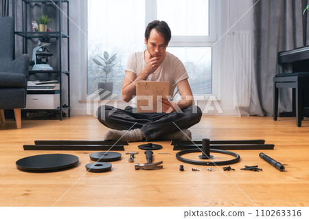 The man is intently studying the instructions for self-assembly of furniture. 110263316