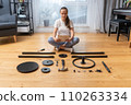 A woman reads instructions while sitting on the floor in a lotus position. 110263334
