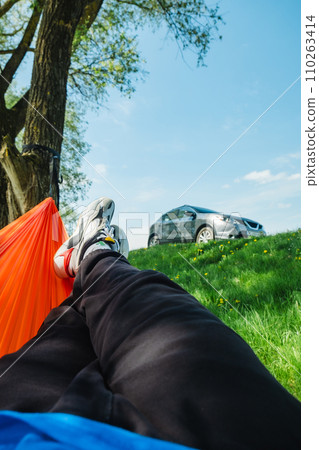 a man rests in a hammock overlooking a parked car on a green lawn in nature 110263414