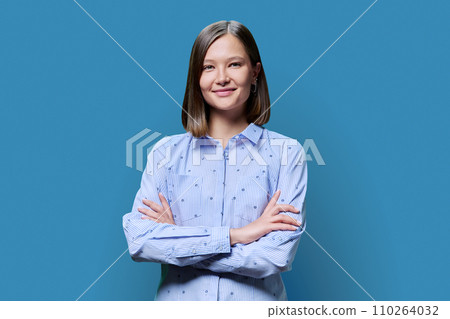 Portrait of confident young woman with crossed arms on blue background 110264032