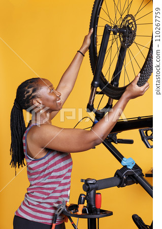 Energetic african american female dismantling damaged bicycle tire to repair and replace with new. Youthful athletic black woman grasping and carrying bike wheel for further maintenance. 110267759