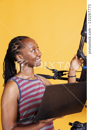With the use of specialized work tools and laptop, focused black woman fixes damaged bicycle. Youthful african american woman searching the internet on wireless computer for new bike components. 110267773
