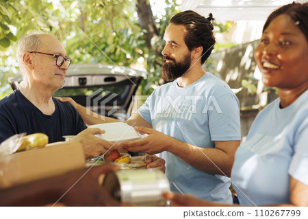 Close-up of multiethnic volunteers, including a smiling woman, distribute donations of food to the needy, offering help and hope to homeless people. Caring charity workers aiding the less privileged. Close-up of multiethnic volunteers, including a smiling woman, distribute donations of food to the needy, offering help and hope to homeless people. Caring charity workers aiding the less privileged. 110267799