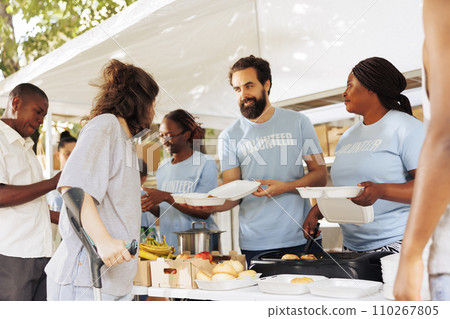 Multiethnic group of volunteers provides aid, handing out free food to disadvantaged communities. They support homeless, sick, and those in poverty. Charitable act of compassion and relief. Multiethnic group of volunteers provides aid, handing out free food to disadvantaged communities. They support homeless, sick, and those in poverty. Charitable act of compassion and relief. 110267805