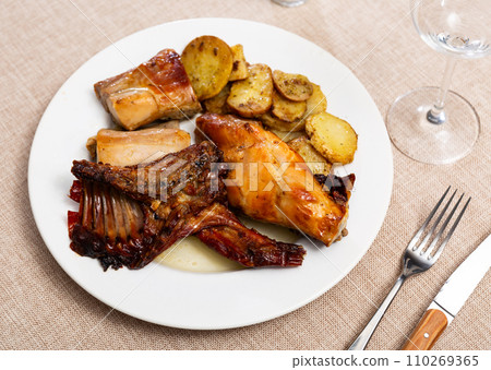 Lunch is served on plate - pieces of young rabbit baked with slice of potato. Close-up 110269365