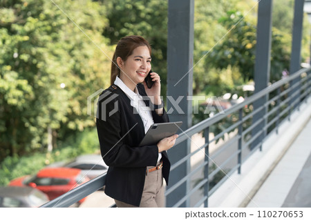 Young Asian business woman wearing suit using smartphone standing on city street outdoors Young Asian business woman wearing suit using smartphone standing on city street outdoors 110270653