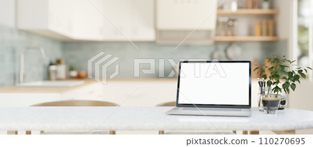 Home workspace, a white-screen laptop computer on a white dining table in a modern bright kitchen. Home workspace, a white-screen laptop computer on a white dining table in a modern bright kitchen. 110270695