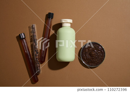 Minimal concept for advertising organic product for skin and body care. On a brown background, a green bottle displayed with coffee ingredient on test tubes and petri dish. Top view, space for design Minimal concept for advertising organic product for skin and body care. On a brown background, a green bottle displayed with coffee ingredient on test tubes and petri dish. Top view, space for design 110272396