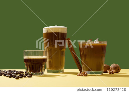 Different delicious cups of coffee with creamy foam decorated on a green background with coffee beans, cinnamon sticks and walnuts. A cup of coffee in the morning helps you feel more alert and active 110272428