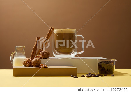 Background of the drink advertisement helps to keep the spirit awake. Cup of coffee with beans, cinnamon sticks, walnut and milk on brown background. Coffee has become a popular drink in Vietnam Background of the drink advertisement helps to keep the spirit awake. Cup of coffee with beans, cinnamon sticks, walnut and milk on brown background. Coffee has become a popular drink in Vietnam 110272431