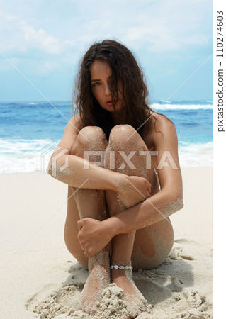 Beautiful young woman in sand on the beach. Sexy girl in Bikini sitting near sea Beautiful young woman in sand on the beach. Sexy girl in Bikini sitting near sea 110274603