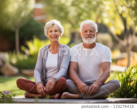 Smiling seniors elderly couple sits cross-legged in sunny garden. Pensioners man and woman wear comfy yoga clothes 110276418
