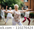 Joyful senior women engage in a tai chi yoga class outdoors, with a focus on the beaming lady in floral in the foreground 110276424