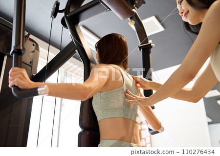 Woman training her back with a pec deck machine Woman training her back with a pec deck machine 110276434