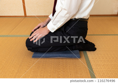 A man wearing a white shirt sitting on a cushion 110276496
