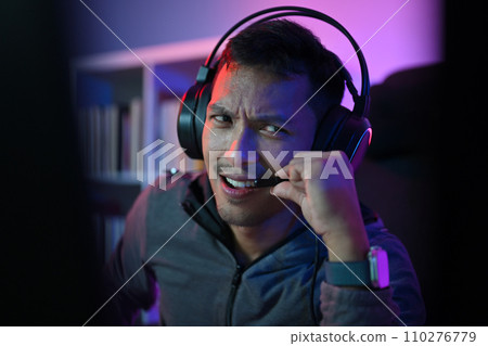 Asian male gamer playing online video game on pc and talking with players on chat through microphones. 110276779