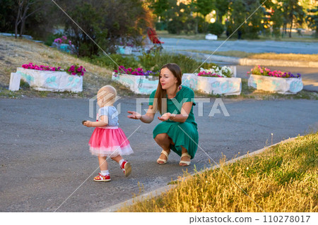Cute mother with a charming baby daughter walks in the city park Cute mother with a charming baby daughter walks in the city park 110278017