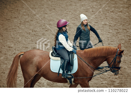 Aerial, top view. Female teacher, instructor teaching little girl, kid horseback riding. Outdoor lesson Aerial, top view. Female teacher, instructor teaching little girl, kid horseback riding. Outdoor lesson 110278022