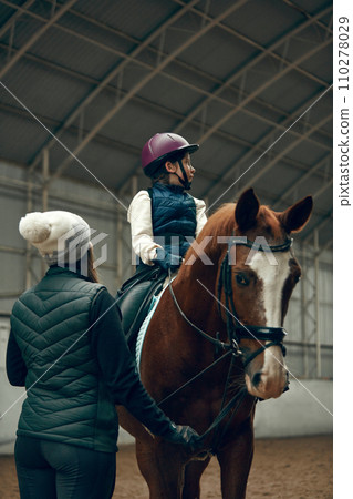 Female instructor teaching little girl, child horseback rising. Kid practicing trail riding, dressage Female instructor teaching little girl, child horseback rising. Kid practicing trail riding, dressage 110278029