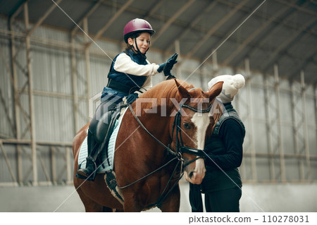 Good lesson,. Little girl giving high five to her instructor. Learning horseback riding on special arena Good lesson,. Little girl giving high five to her instructor. Learning horseback riding on special arena 110278031