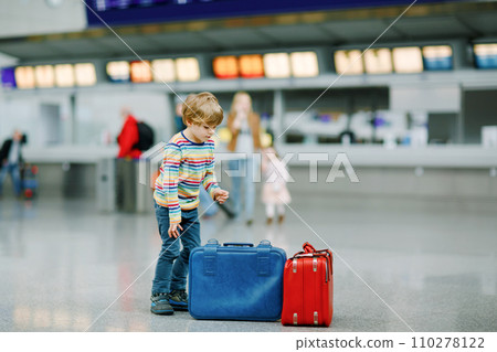 Cute little kid boy with luggage, two suitcases on international airport. Mother with little girl daughter on background, Happy family wating for flight and going on vacations. Travel lifestyle. 110278122
