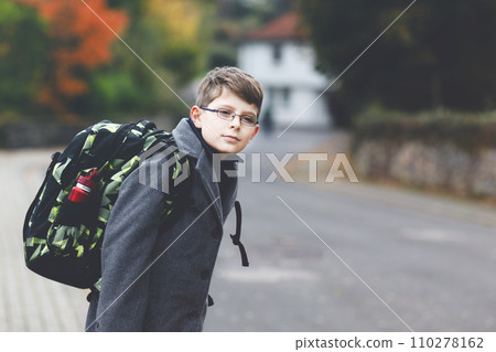 Happy kid boy with glasses and backpack or satchel. Schoolkid in stylish fashon coan on the way to middle or high school on cold autumn day. Healthy child outdoors on the street, on rainy day. Happy kid boy with glasses and backpack or satchel. Schoolkid in stylish fashon coan on the way to middle or high school on cold autumn day. Healthy child outdoors on the street, on rainy day. 110278162