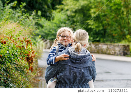 Mom holds her little daughter on hands standing under umbrella. Mother and happy preschool girl, child with eyeglasses on rainy day on the street. Happy family. 110278211