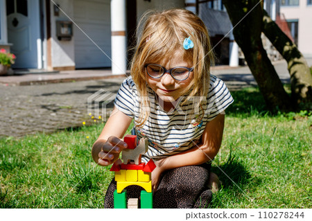 Little preschool girl playing with wooden blocks on the table outdoors. Educational game for small children. Happy child builds a tower from wooden rainbow stacking blocks. Little preschool girl playing with wooden blocks on the table outdoors. Educational game for small children. Happy child builds a tower from wooden rainbow stacking blocks. 110278244