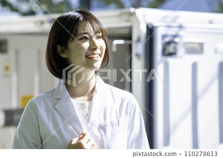 A woman in a white coat standing in front of a truck 110278613