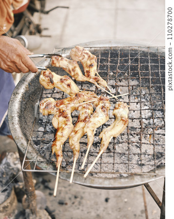 Man grills chickens over an charcoal stove. Man grills chickens over an charcoal stove. 110278700